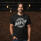 MAN WEARING Black t-shirt with 'Bad Co' logo on a white background BCO501S, BCO501M, BCO501L, BCO501XL, BCO501XXL, BCO501XXXL, BCO501XXXXL, BCO501XXXXXL